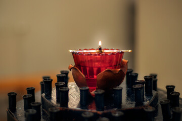 A burning wick in a red glass lamp in a church candlestick without candles. Black church candle holder. Blurred background and foreground.