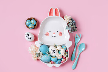 Easter table setting decoration with cute plate in the shape of a bunny with  Easter eggs and candy on pink background. Happy Easter concept. Idea for Easter dinner