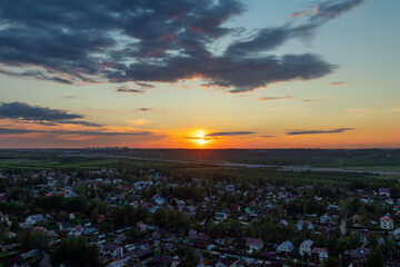 A view from a height of a large village on the background of a sunset with clouds. A motorway is visible in the distance. High-rise buildings are visible in the distance. Lots of clouds. Summer.