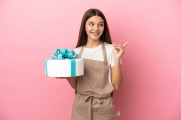 Little girl with a big cake over isolated pink background intending to realizes the solution while lifting a finger up