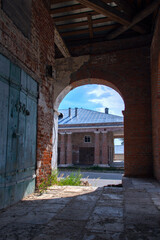View through the brick arch to the building of the shopping mall with columns. Closed doors. The walls and columns are made of red brick. Summer. In the shadows. Hard daylight.