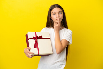 Little girl holding a gift over isolated yellow background having doubts while looking up