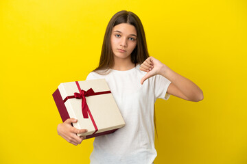 Little girl holding a gift over isolated yellow background showing thumb down with negative expression