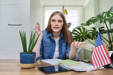 Young female student looking at the camera, USA flag on the table.