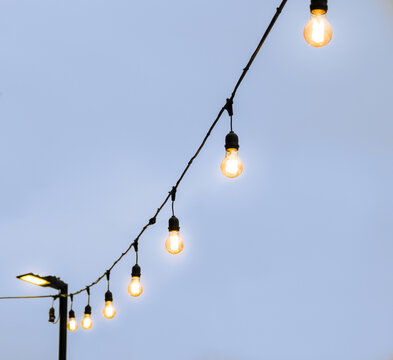 Close up of anging antique edison style filament light bulbs on wire with blurry background. Industrial pendant glowing lamps near cafe at street, isolated.