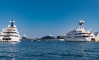 Fototapeta na wymiar A lot of huge yachts are in port of Monaco at sunny day, Monte Carlo, mountain is on background, glossy board of the motor boat, megayachts are moored in marina, sun reflection on glossy board