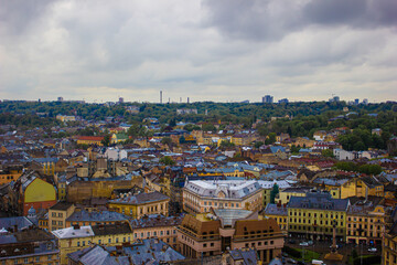 Fototapeta na wymiar Lviv, old city view, with blue sky and fluffy clouds, summer. Aerial drone view of urban landscape, small buildings and trees. Background in the light fog or aerial perspective.