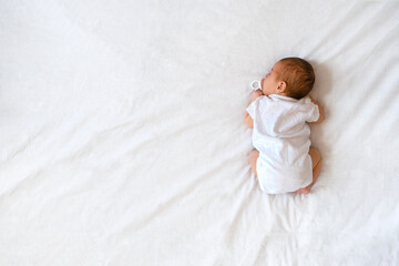Top view of cute adorable newborn baby wearing white body sleeping on stomach