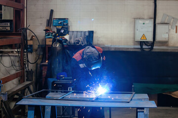 Factory worker in protective mask welding iron parts
