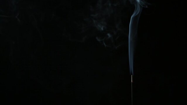 Flowing smoke from incense stick against black background	
