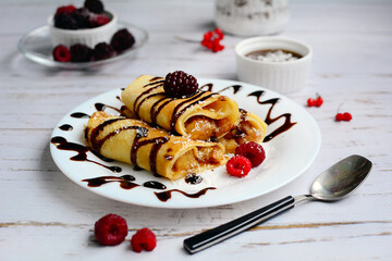 Pancakes with chocolate and berries on a white plate on a light wooden background. Breakfast