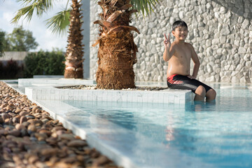 Asian Young Boy Having a good time in swimming pool, He Jumping and Playing a Water in Summer.