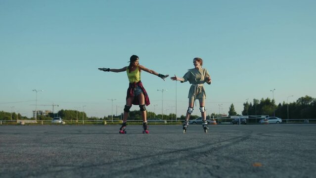 Happy young pretty girls rolling skating outdoors having fun hold hands each other sport street legs friends rollerblading activity close up slow motion