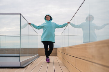 Portrait caucasian woman in mint hoodie near glass railing outdoors. 