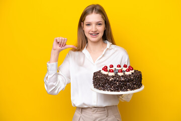 Teenager Russian girl holding birthday cake isolated on yellow background proud and self-satisfied