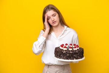 Teenager Russian girl holding birthday cake isolated on yellow background with headache