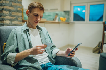 Redhead man shopping online with credit card and a smartphone at home