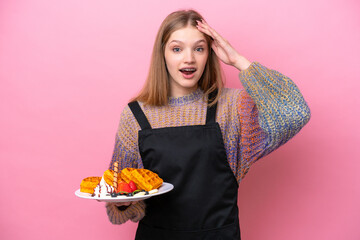 Teenager Russian girl holding a waffles isolated on pink background with surprise expression