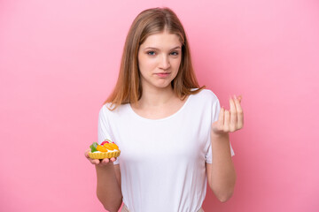 Teenager Russian girl holding a tartlet isolated on pink background making money gesture