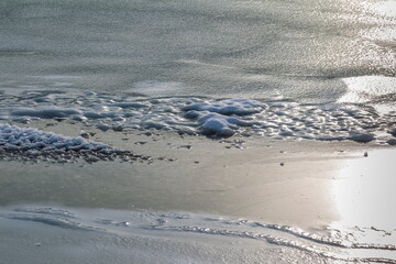 White ice crystals close-up on the dark strip of the main ice of the river in winter
