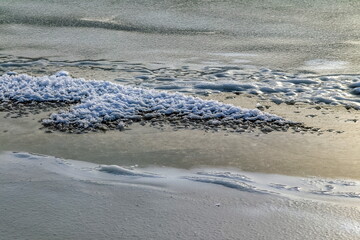 White ice crystals close-up on the dark strip of the main ice of the river in winter