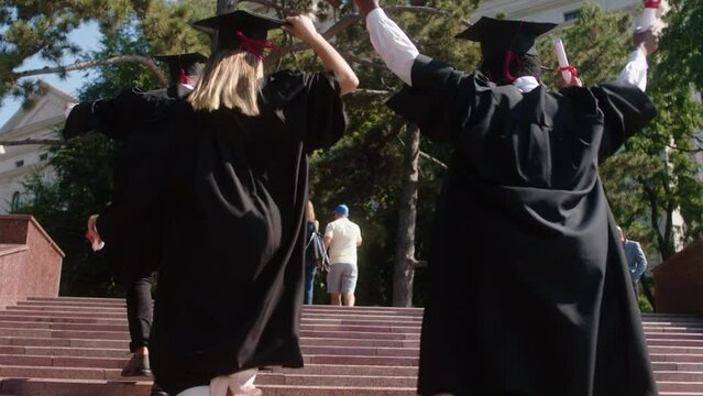 Excited Multiracial Group Of Graduates Students Running Up The Stairs Outside Of The College Building They Wearing Graduation Caps And Holding Diplomas In Hands