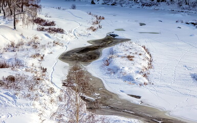 Winter landscape with a fast river with ice-free water, snow, dry grass