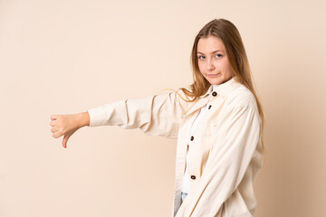 Teenager Ukrainian girl isolated on beige background showing thumb down with negative expression
