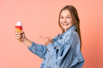 Teenager Ukrainian girl with a cornet ice cream isolated on pink background and pointing it