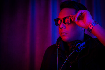 Young latin man with sunglasses portrait under red and blue lights.