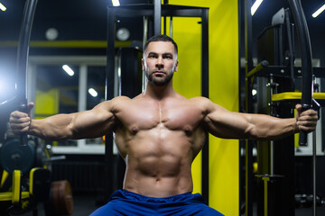 Fototapeta na wymiar Attractive bodybuilder is working out in a gym training his chest muscles using sports equipment
