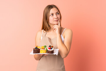 Pastry Ukrainian chef holding a muffins isolated on pink background thinking an idea