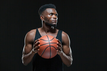 Portrait of afro american male basketball player playing with a ball over black background. Fit...