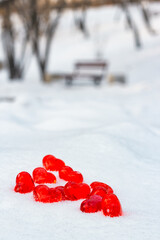 Closeup set of small bright red glass hearts on powdery snow of snowdrift at cold winter day in park, symbol of romantic love, St. Valentine's Day holiday concept, vertical image with low angle shoot