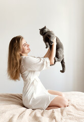 a sexy girl in thin pajamas sits on the bed and holds a beautiful Scottish cat. sexy girl at home in pajamas on a bed with a pet