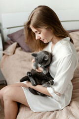 a sexy girl in thin pajamas sits on the bed and holds a beautiful Scottish cat. sexy girl at home in pajamas on a bed with a pet.girl playing with cute cat