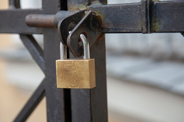A large golden lock hangs on an iron door in close-up. The gate is bolted. Production of gate...