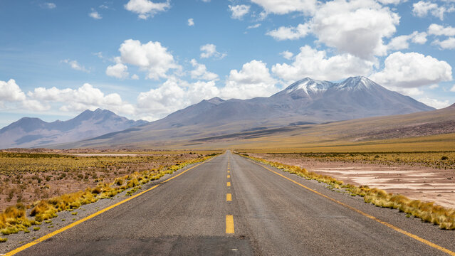Asphaltierte Stra&szlig;e f&uuml;hrt durch die Atacama W&uuml;ste entlang gr&uuml;ner steppen, roter Sandlandschaften sowie riesiger Vulkane und schneebedeckter Berge