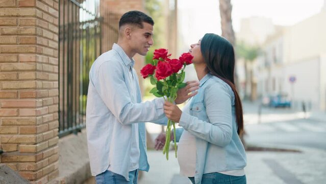 Young latin couple smiling confident suprise with bouquet of roses at street