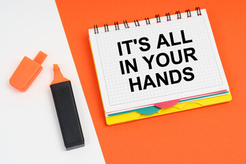 On a white-orange surface lies a marker and a notepad with the inscription - IT IS ALL IN YOUR HANDS