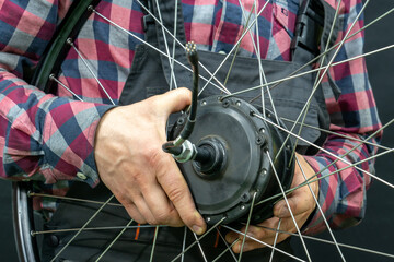 Repair of electric bicycles. A bicycle mechanic holds a wheel with an electric motor in his hands....