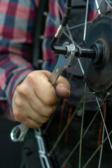 Obraz premium Repair of electric bicycles. A bicycle mechanic holds a wheel with an electric motor and a wrench in his hands. Bicycle wheel close-up on a black background.