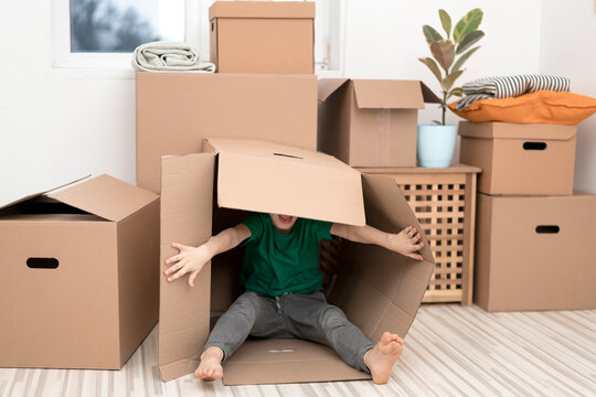 Excited little boy jumping inside a huge cardboard box. He is playing and looking out of a box. Kid is happy about moving into a new home.