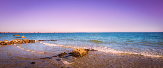 Purple sky and blue ocean with rocks and gentle waves rolling in on the beach on Cape Cod. Winter coastal landscape at sunset.