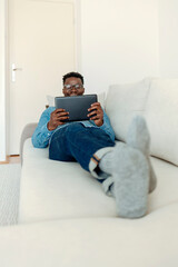 Millennial african-american guy chatting with friends on smartphone, lying on bed at home, copy space. Man using smartphone at home.