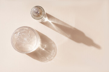 Cosmetics and liquid gel mask for care on a beige background. Shadows and glowing reflections from bottles.