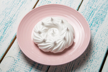 One large meringue on a pink saucer. Home confectionery. Old retro white and blue table.