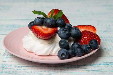 Pavlova cake with strawberries and blueberries and mint on a pink platter. Home confectionery. Old retro white and blue table.
