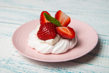Pavlova cake with strawberries and mint on a pink platter. Home confectionery. Old retro white and blue table.
