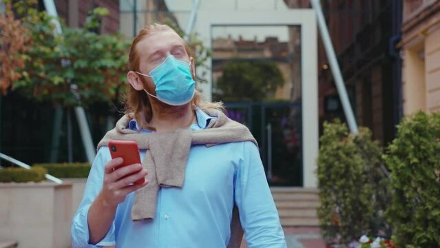 Tourist caucasian man exploring city center traveling alone using smartphone navigation application wearing preventive fave mask against coronavirus. Pandemic. Tourism.